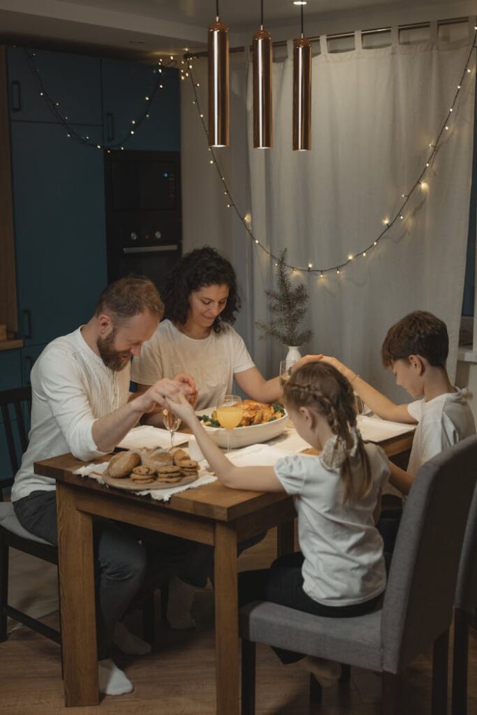 A family holding hands and praying around a festive dinner table set with food and decorations.